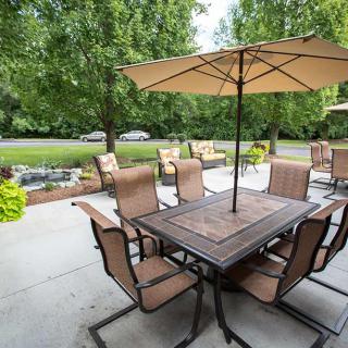 A well-furnished patio with a table, chairs, and umbrellas in a garden setting.