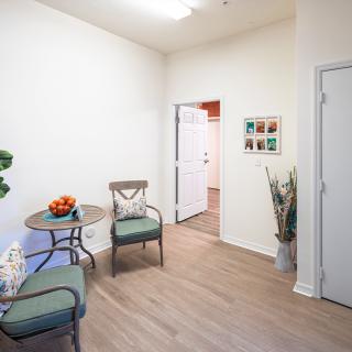 A cozy waiting room with chairs and a small table, decorated with plants and art on the wall.