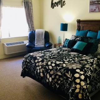 A cozy bedroom with floral bedding, a cushioned chair by the window, and decorative pillows.