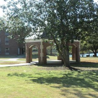 A brick gazebo in a park surrounded by trees and grass.