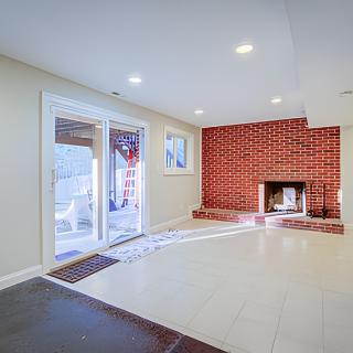 A spacious living room featuring a brick fireplace, large windows, and tile flooring.