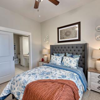 A cozy bedroom featuring a queen-sized bed with floral bedding, flanked by nightstands with lamps, and a ceiling fan overhead.