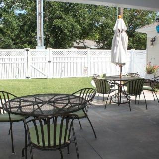 A backyard patio with metal tables and chairs, surrounded by a white fence.