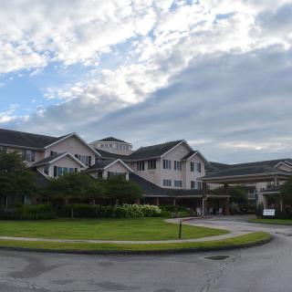 A large residential building with a circular driveway and cloudy sky above.