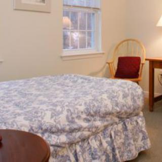 A cozy bedroom with a bed, chair, and lamp near a window.