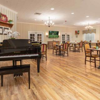 A warmly lit dining area featuring a piano, wooden floors, and neatly arranged tables and chairs.