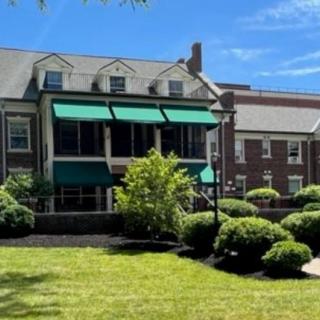 A picturesque house with green awnings, surrounded by lush greenery on a sunny day.