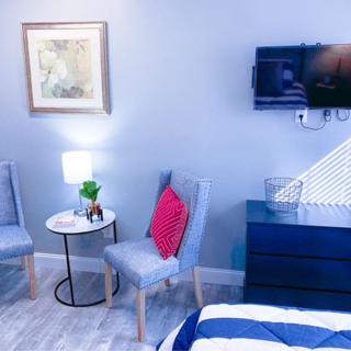 A modern bedroom interior with chairs, a small table, and a wall-mounted TV.