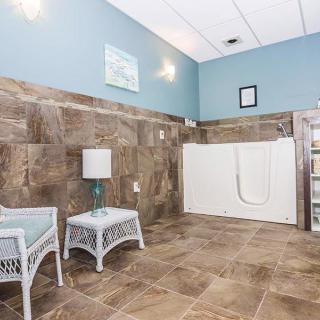 A spacious bathroom with a walk-in tub, featuring tile walls and floor, light blue walls, and wicker furniture.