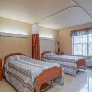 A hospital room with two neatly made beds and a curtain divider.