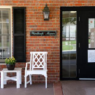 The welcoming entrance of Woodlawn House featuring white furniture and a brick facade.