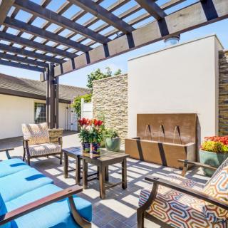 A stylish patio with comfortable seating under a pergola, adorned with colorful cushions and decorative flowers.
