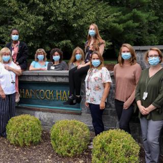 A group of people wearing masks gathered outdoors in front of a sign.