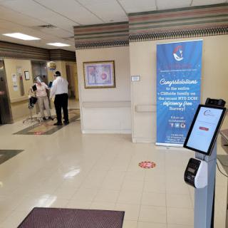 A lobby area featuring an information kiosk, a congratulatory banner, and people waiting near the elevator.