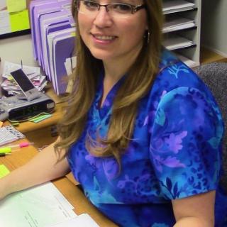 A woman wearing glasses sits at an office desk with documents.