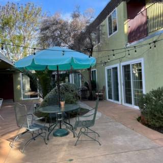 A sunny backyard patio featuring a table with chairs and an umbrella, adorned with string lights.