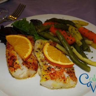 A delicious plate featuring seasoned fish with citrus garnish, accompanied by a medley of mixed vegetables.