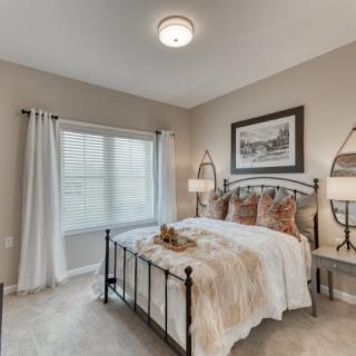 A cozy bedroom with neutral tones, featuring a neatly made bed, bedside lamps, and a large window.