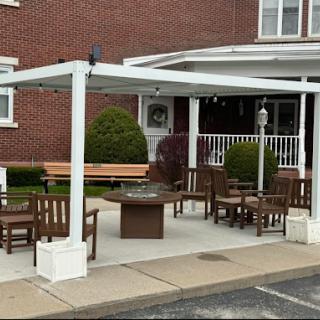 A cozy outdoor seating area featuring a fire pit, surrounded by comfortable furniture and shaded by a pergola.