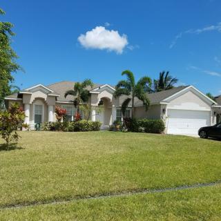 A suburban house with palm trees and a well-maintained lawn under a blue sky.