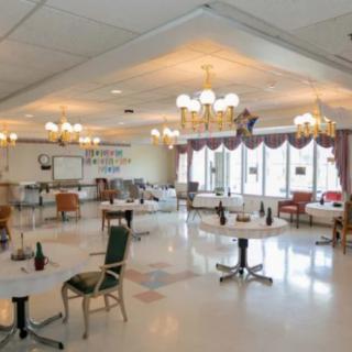 An empty dining area with tables and chairs, illuminated by chandeliers.