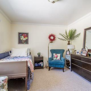 A cozy bedroom with a bed, armchair, dresser, and decorative elements.