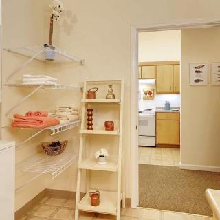 A cozy bathroom with neatly organized shelves and a view into the kitchen.