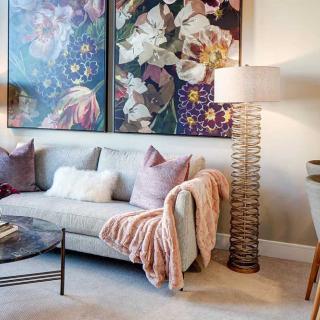A cozy living room featuring stylish artwork, a comfortable sofa with accent pillows and a throw, accompanied by a unique floor lamp and glass coffee table.