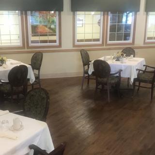 An empty dining room with neatly set tables and chairs, featuring large windows.