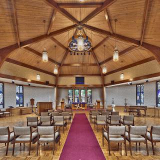 A beautifully designed interior of a ceremony space featuring wooden beams, ample seating, and soft lighting.