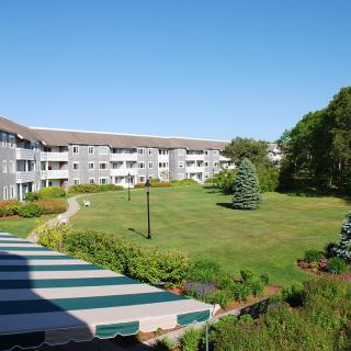 A scenic view of an apartment complex with a well-maintained lawn and garden on a sunny day.