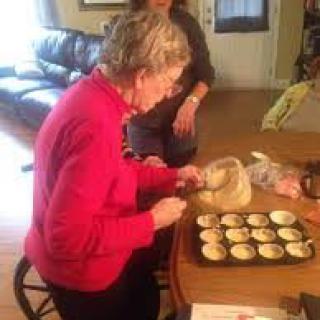 An elderly woman preparing cupcakes in a cozy kitchen setting.