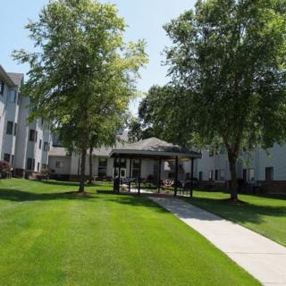 A view of an apartment building with a well-maintained lawn and surrounding trees.