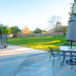 A spacious backyard with a patio set and umbrella overlooking a green lawn and trees.