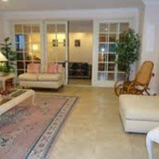 A cozy living room with sofas, a rocking chair, a rug, and indoor plants, featuring glass doors leading to another space.