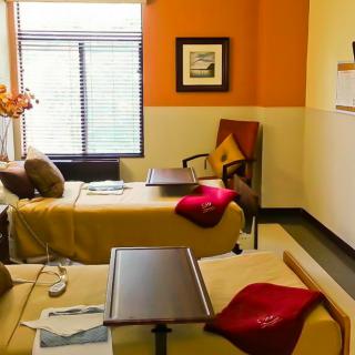 A cozy hospital room with two patient beds, equipped with rolling tables and decorated with bright accents and natural light.