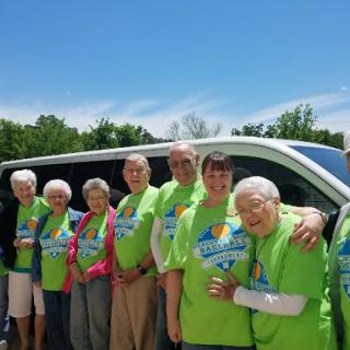A cheerful group of seniors dressed in bright green shirts poses together outdoors, ready for their next adventure.