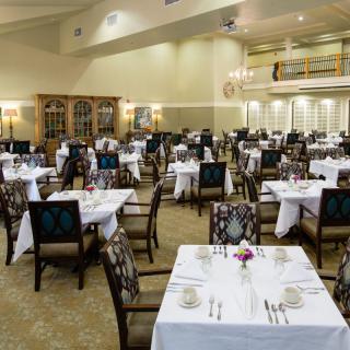 A spacious and elegantly decorated restaurant interior with neatly arranged tables and chairs, each adorned with white tablecloths.