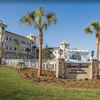 A scenic view of a large building with palm trees and a sign in front, set against a clear blue sky.