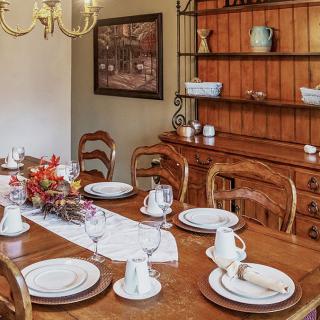 An elegantly set dining table with wooden chairs and china, accented by a decorative shelf and chandelier.