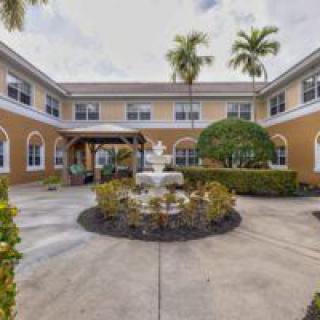 A courtyard with a central fountain, surrounded by lush landscaping and a two-story building with palm trees.