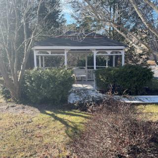A charming gazebo surrounded by lush greenery, illuminated by sunlight.