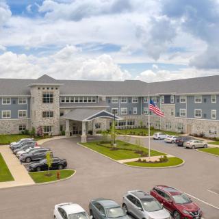 A large building with a parking lot and cars, featuring an American flag and a cloudy sky in the background.