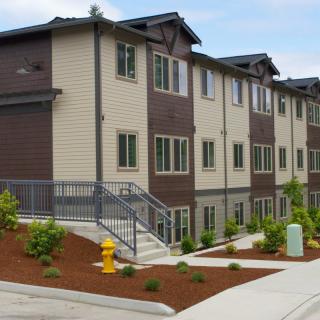 A modern apartment building with landscaped surroundings and a staircase leading to the entrance.