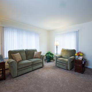 A cozy living room with a sofa, armchair, and large windows.