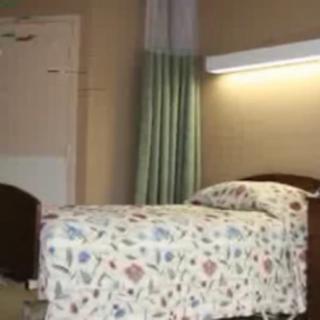 A tidy hospital room with a single bed and decorative bedding under gentle ambient lighting.