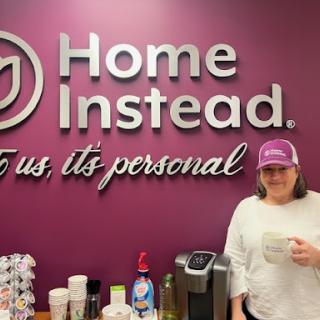An employee standing in front of the Home Instead office sign, showcasing a welcoming environment.