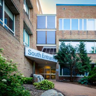 The south entrance of a modern brick building, featuring large windows and surrounding greenery.