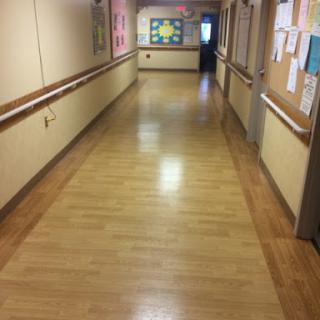 A view of a well-lit hallway with wooden flooring and bulletin boards along the walls.