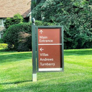 A directional sign indicating the main entrance and various villas in a well-manicured outdoor area.